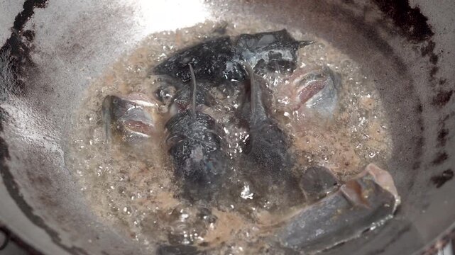 Close-up of catfish being fried in a pan. The hot oil bubbles as the fish cooks.