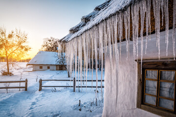 Icicles are hanging on thached straw roof of old village house at winter sunset