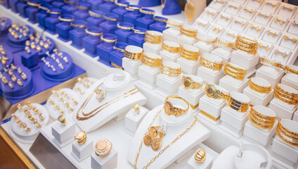 Display of assorted gold jewelry including necklaces, bracelets, and earrings arranged on white stands with blue boxes in a jewelry store setting © Dasha Petrenko