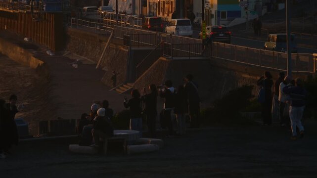 Evening seaside scene at Enoshima where people stand quietly facing the colorful sunset sky.