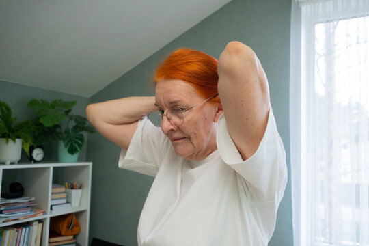 A seventy year old senior woman performs a warm-up exercise with lifted arms, specifically targeting the neck and shoulder region. This gentle movement aids flexibility