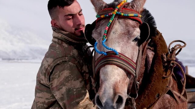 Close-up view of a man standing beside his horse in winter. Detailed bridle and calm expression highlight the bond between human and animal in a rural natural setting.