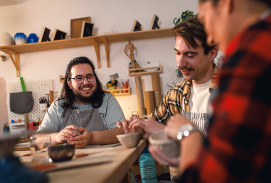 Man with his friends attending pottery class havng fun making clay objects together.