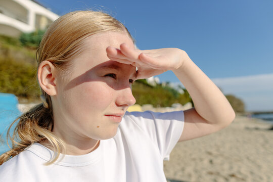 Close up portrait of teen girl shielding eyes from bright sun while looking into distance on beach. Vision, future goals and confident youth lifestyle by seaside.

