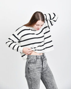 unge Frau im gestreiften Pullover und grauer Jeans blickt auf ihren Bauch. Modernes Fashion-Portr&auml;t mit nat&uuml;rlicher Pose &ndash; Lifestyle, Body Awareness und Casual Style.