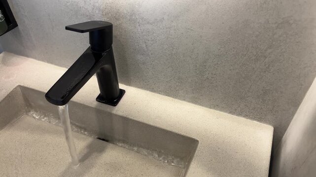 Water running from a black faucet into a white sink in a modern bathroom. Hygiene routine, clean interior, minimalist design.