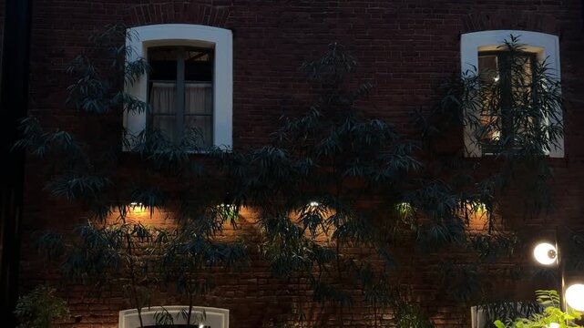 Brick apartment building facade with glowing windows at night, urban residential life, cozy neighborhood, evening calm, city architecture.