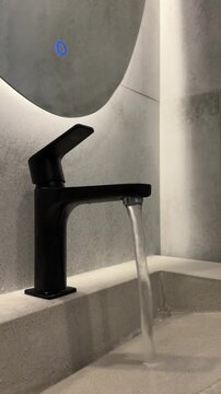 Water running from a black faucet into a white sink in a modern bathroom. Hygiene routine, clean interior, minimalist design.