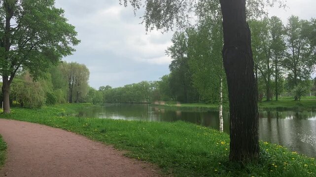 Park path along a calm river with green trees, peaceful nature walk, outdoor recreation, spring landscape, travel background.