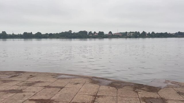 Calm lake with a stone waterfront promenade and distant town skyline, peaceful travel scenery, lakeside relaxation, outdoor landscape, quiet getaway.