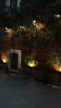 Brick courtyard with a small doorway and warm garden lights at night, cozy outdoor design, home privacy, urban lifestyle, evening calm.