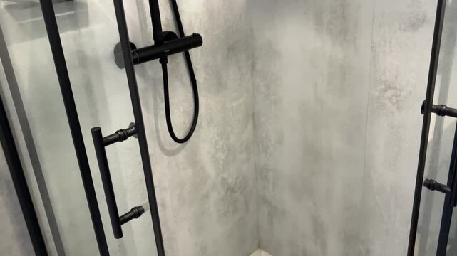 Black shower faucet and hose on a concrete wall behind glass in a modern bathroom, clean interior, hygiene routine, minimalist home design.