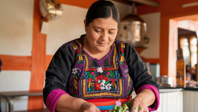 A focused indigenous woman wearing beautiful traditional embroidered clothing prepares a fresh meal in a bright rustic kitchen, capturing cultural heritage.
