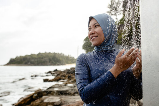 Filipina woman in a light blue headscarf standing beneath an outdoor shower