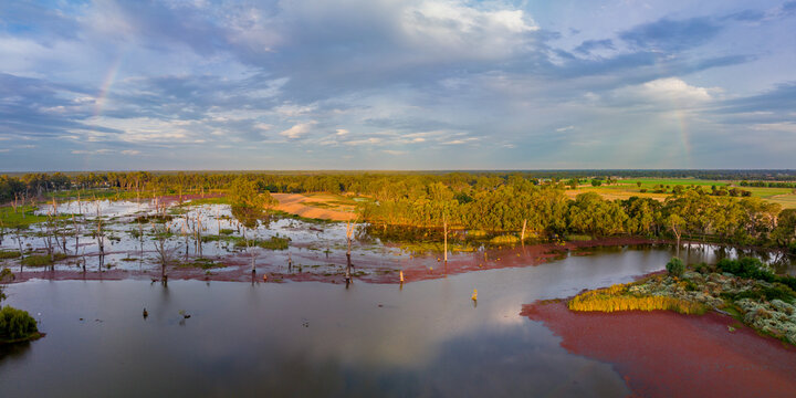 Aerial panorama view of a faint rainbow in a dramatic sky over wetlands in golden evening light