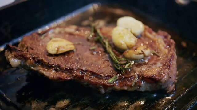 Cooked steak browning in a grill pan while being basted with melted butter and herbs