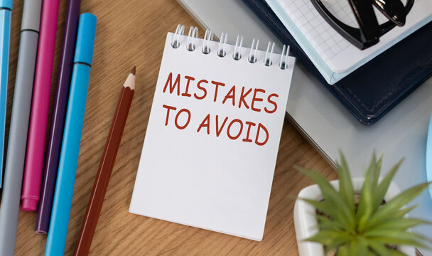 MISTAKES TO AVOID text written in red on a spiral notepad on a wooden desk with office supplies.