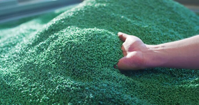 Hand holding green plastic polymer granules for industrial manufacturing