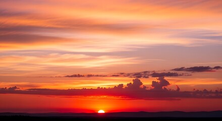 Obraz premium Vibrant orange and pink sunset sky with wispy clouds over a dark horizon line