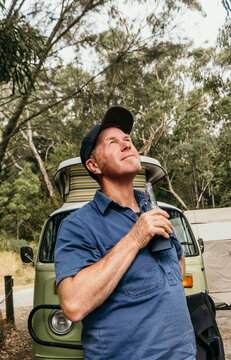 Man in front of camper van enjoys a beer with a smile.