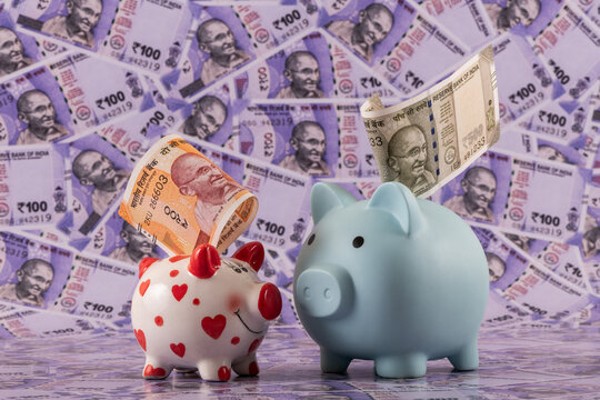 Two piggy banks against a background of Indian rupees