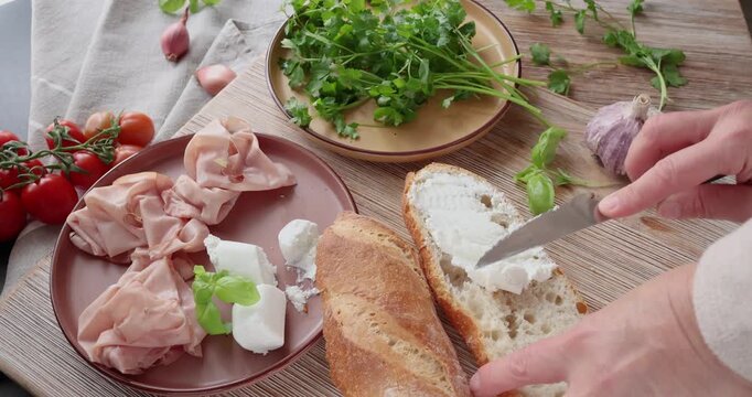 Anonymous person prepares sandwich with cheese, basil, and mortadella in kitchen. Italian cuisine, high-quality farm-to-table ingredients.