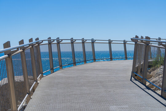 A fenced boardwalk made of steel winding away toward a distant blue ocean