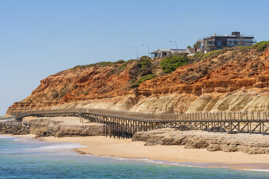 Distant view of a coastal walkway above sandy beach and around the base of eroded cliffs