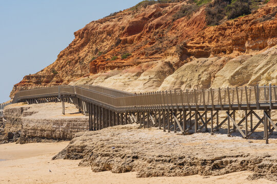 Distant view of a coastal walkway above a sandy beach and around the base of eroded cliffs