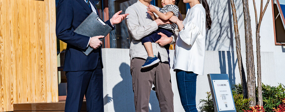 スーツの営業マンが家族（夫婦と子供）に新築住宅を案内しているシーン