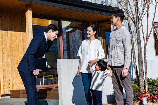 スーツの営業マンが家族（夫婦と子供）に新築住宅を案内しているシーン