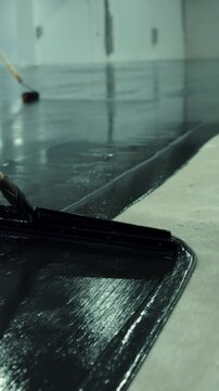 Construction worker applying black epoxy resin to concrete floor