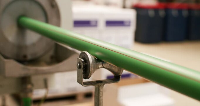 Close up of green plastic pipe moving on roller during production process