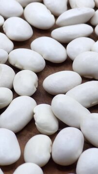 White dry organic butter beans scattered on a wooden surface, vertical video
