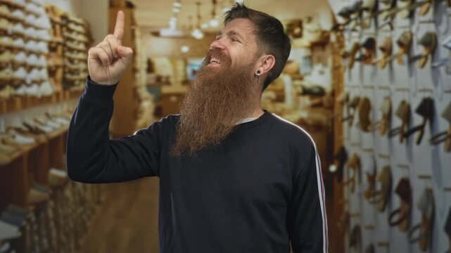 Young bearded man pointing both index fingers upward at a shoe display in an indoor shoe store with wooden shelves; excitement.