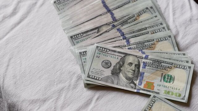 Stack of one hundred dollar bills is being thrown on a white textured surface. The indoor setting reflects financial success and prosperity.