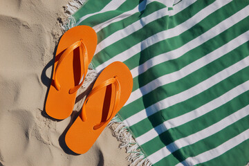 Flip flops, orange and beach towel on sand for summer, vacation and relaxation. Footwear, leisure and outdoor activity for sunny day at seaside.