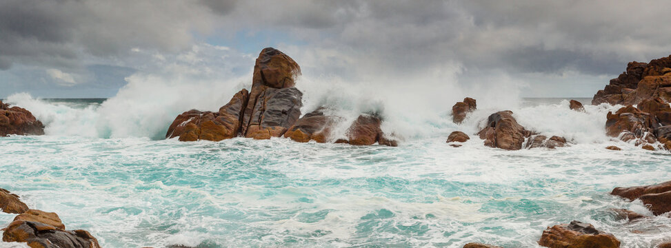 Large ocean waves crashing over coastal rock formations under a dark stormy sky