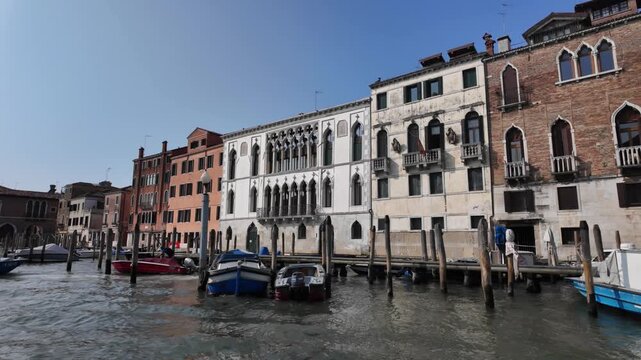 View of Venice from a boat on a sunny day. Ancient buildings and boats can be seen passing by on either side.