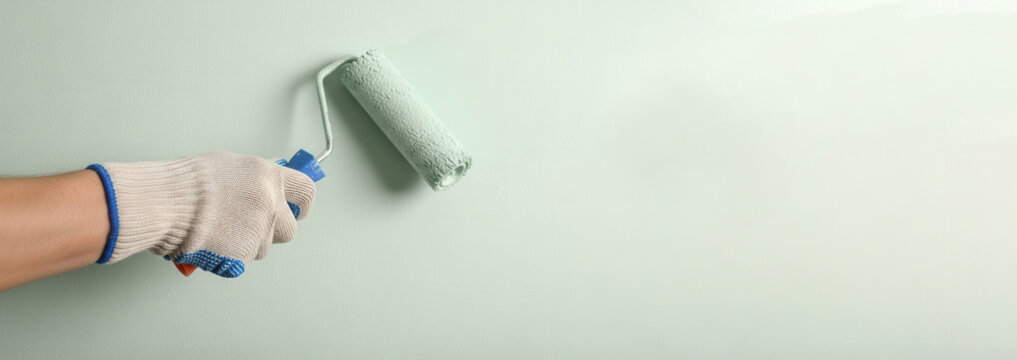 Gloved hand rolling metal paint roller on flat wall surface in modern apartment, home renovation and interior refresh