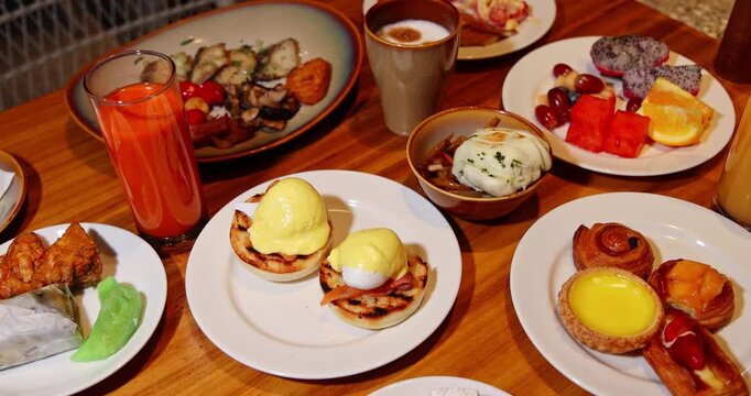 Gourmet breakfast spread sitting on wooden table with Eggs Benedict, fresh juice, pastries, and tropical fruits. luxury hotel, morning meal, healthy lifestyle, brunch, international cuisine, food phot