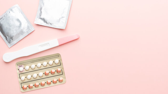Pregnancy test with birth control pills and condoms on pink background. Contraception, family planning, sexual and reproductive health concept.
