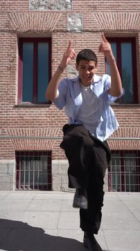 Energetic young man performing hip hop dance moves on a city sidewalk. The stylish dancer showcases his talent with a brick building background