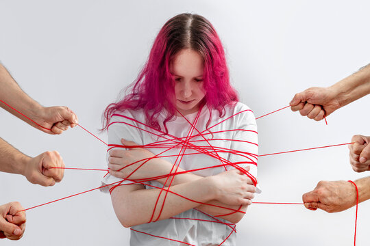 Teen girl tangled in red lines pulled from different sides, concept of manipulation, pressure and judgment, personal boundaries violated, anxiety and avoiding conflict in social environment.
