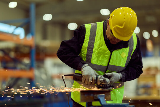 Factory Worker Using Angle Grinder in Industrial Workshop Wearing Hard Hat And High Visibility Vest