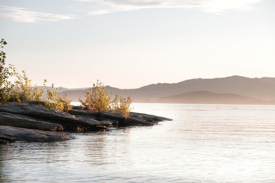 A calm dawn at the Bukhtarma reservoir, East Kazakhstan. In the foreground are the characteristic rocky shores with young vegetation, washed by calm water. 