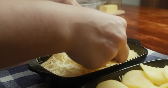 Chef sprinkles grated parmesan cheese over thinly sliced potatoes arranged in baking dishes. Close-up of food preparation, homemade potato casserole, rustic kitchen, natural light, traditional recipe