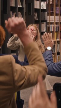 Vertical shot of attendees lifting hands following female writer concluding spoken excerpt during literary presentation inside library