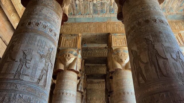 Painted columns and richly decorated ceilings inside the hypostyle hall of the Temple of Hathor at Dendera, Egypt, showcasing textured hieroglyphs and vibrant ancient architectural detail.