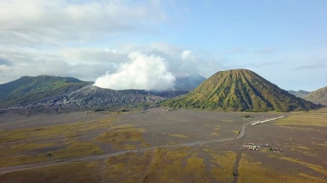 Stunning aerial view of Mount Bromo emitting white smoke alongside Mount Batok in East Java, Indonesia. Majestic volcanic landscape at Bromo Tengger Semeru National Park during a clear morning.